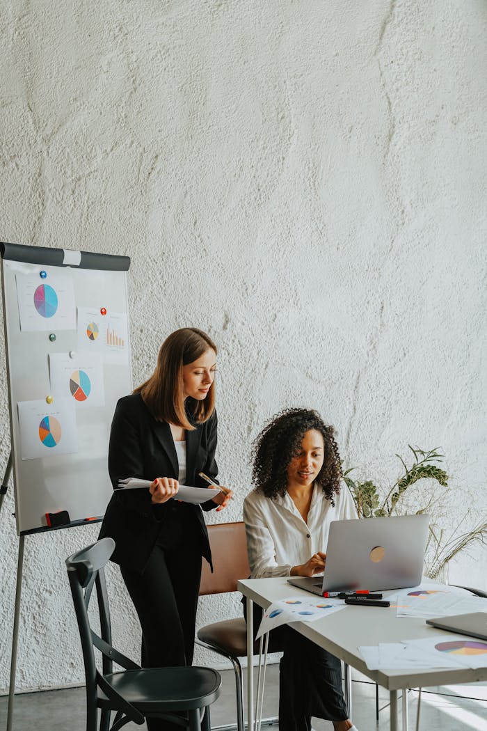 why-choose-us-02 Two businesswomen analyzing graphs on a whiteboard during a meeting.